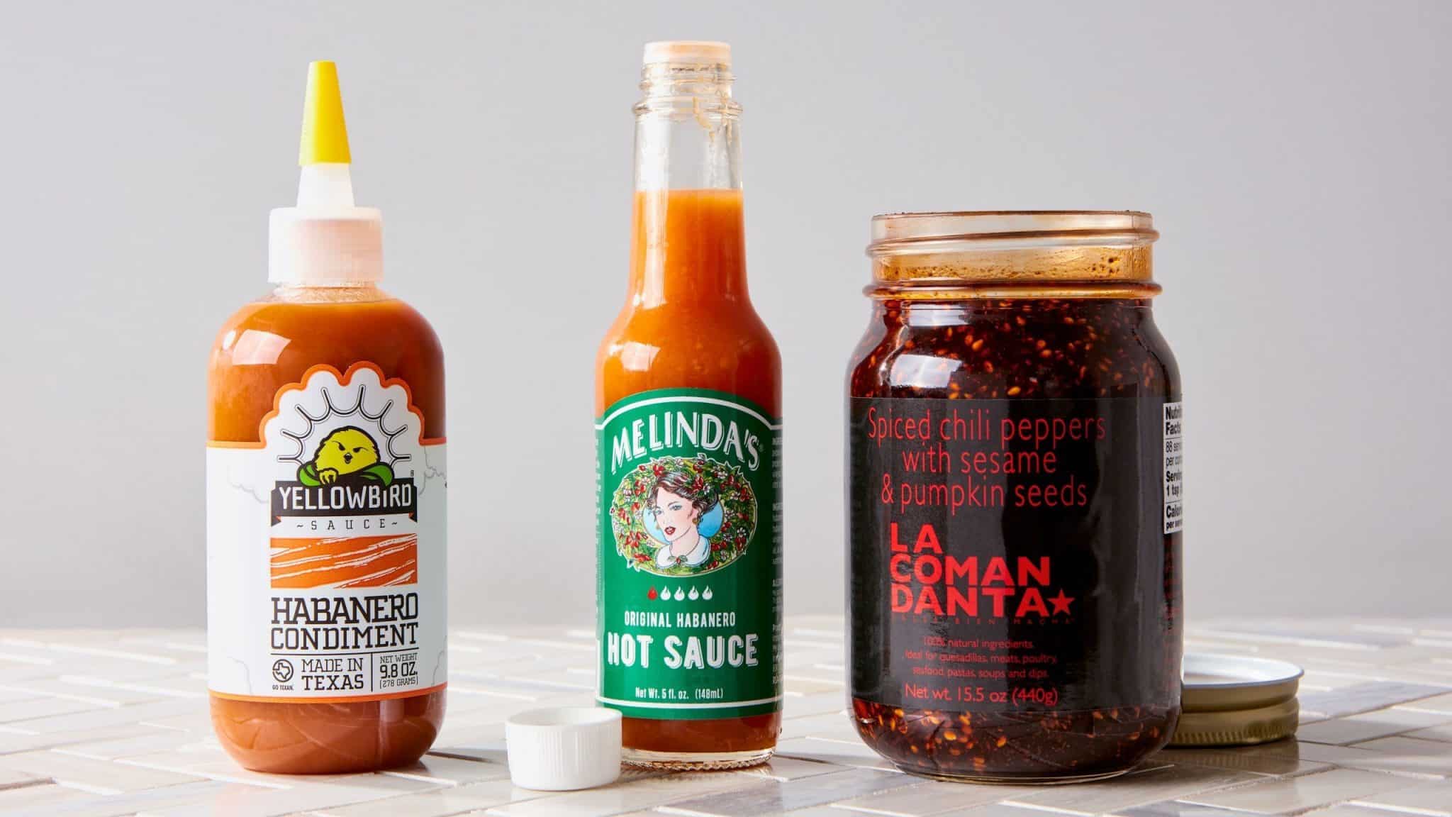 Three hot sauce bottles on a white surface: Yellowbird Habanero Condiment, Melinda's Original Habanero Hot Sauce, and La...