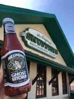 Melinda's Ghost Pepper Ketchup bottle displayed in front of Melinda's restaurant storefront with green roof