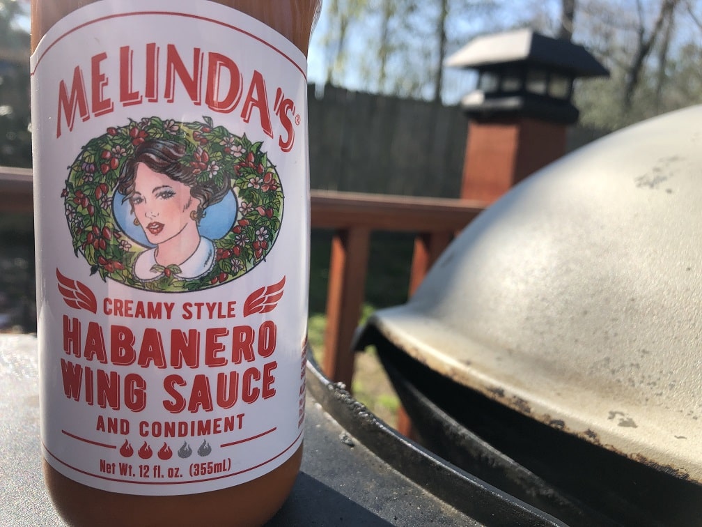 Melinda's Creamy Style Habanero Wing Sauce bottle on outdoor grill, showing woman's portrait logo and product label
