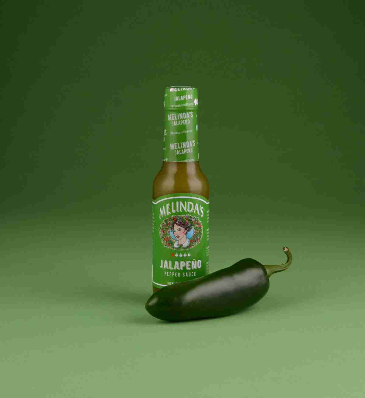 Melinda's jalapeño pepper sauce bottle with fresh jalapeño pepper on green background
