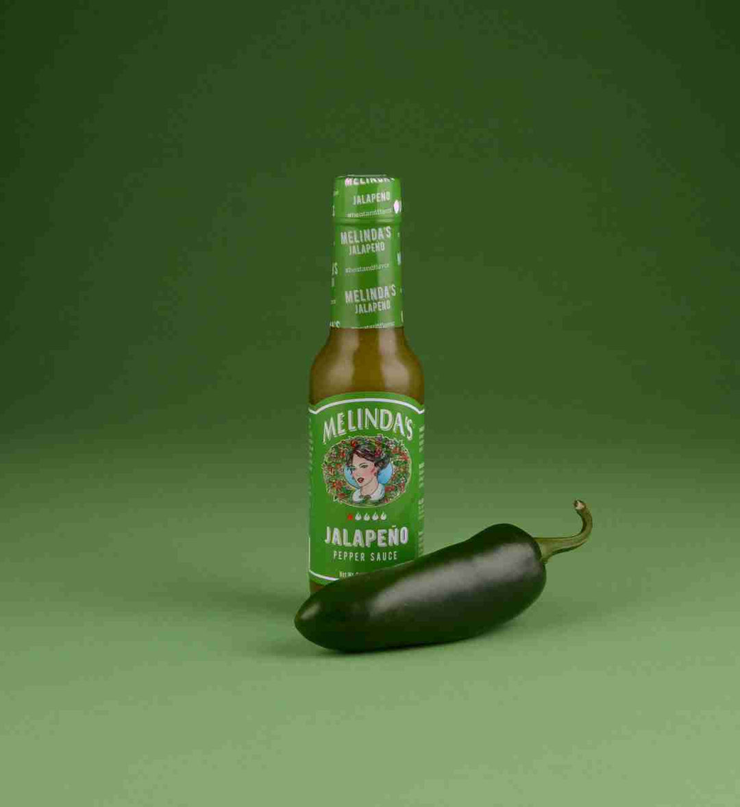Melinda's jalapeño pepper sauce bottle with fresh jalapeño pepper on green background