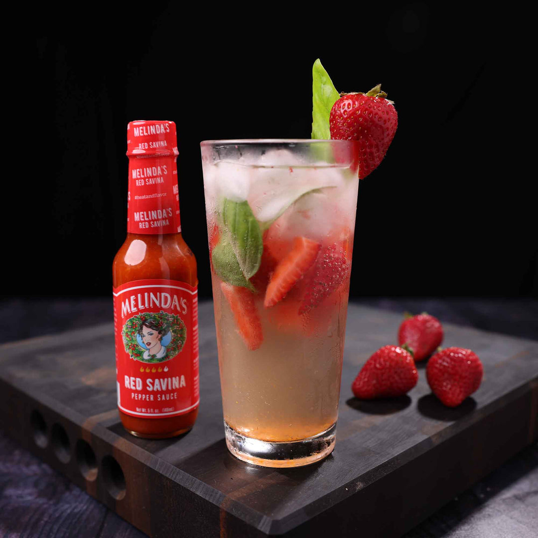 Red Savina pepper sauce bottle next to strawberry basil hard seltzer garnished with fresh strawberry and basil leaf