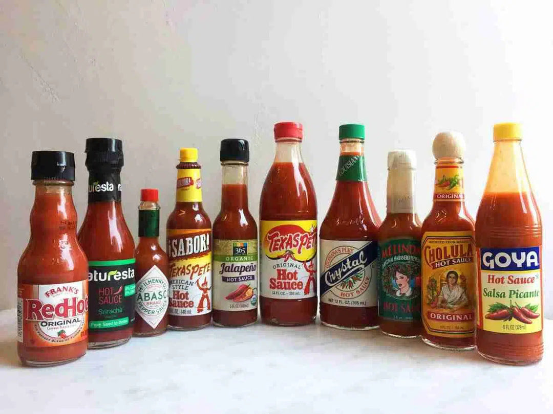 Ten different hot sauce bottles arranged in a row, including brands like Frank's RedHot, Tabasco, Texas Pete, and Goya