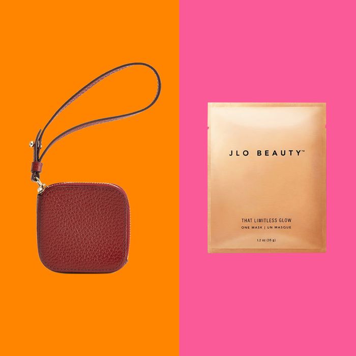 Brown leather wristlet with strap on orange background next to JLO Beauty face mask package on pink background