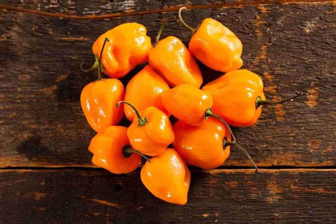 Bright orange habanero peppers scattered on weathered wooden surface, showcasing the main ingredient for spicy hot sauce