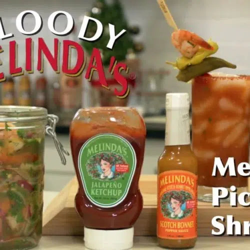 Bloody Mary cocktail garnished with pickled shrimp on skewer, alongside Melinda's jalapeño ketchup and hot sauce bottles