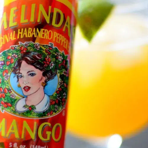 Melinda's Original Habanero Pepper Mango hot sauce bottle next to orange cocktail with lime garnish