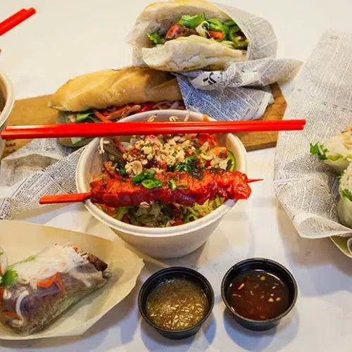 Vietnamese steak vermicelli bowl with grilled meat, noodles, fresh herbs, and spring rolls with dipping sauces on wooden...