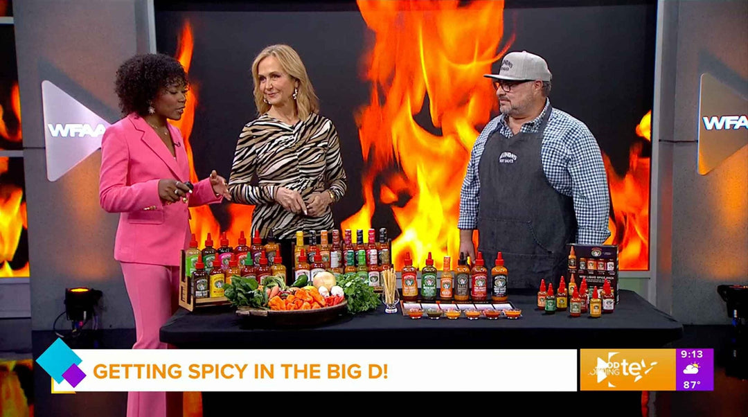 Three people on TV set discussing hot sauce products with flame backdrop and "Getting Spicy in the Big D" text overlay